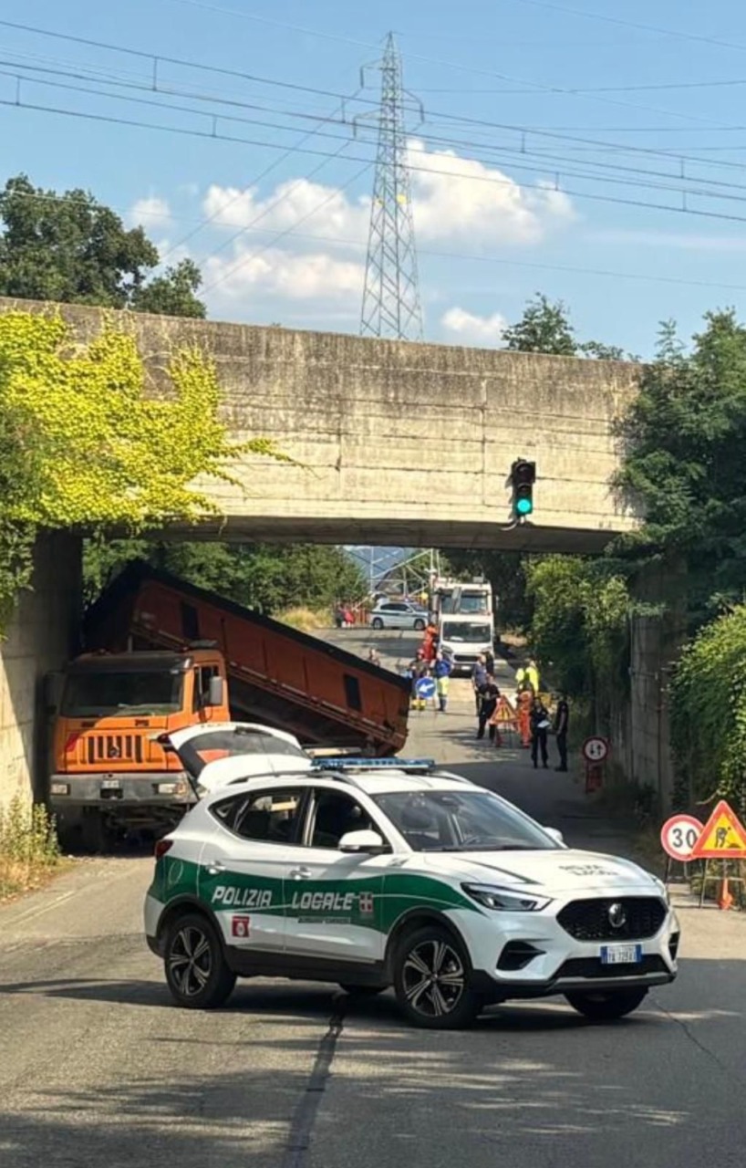 Camion con il cassone alzato si incastra sotto il cavalcavia: traffico in tilt e paura per la ferrovia